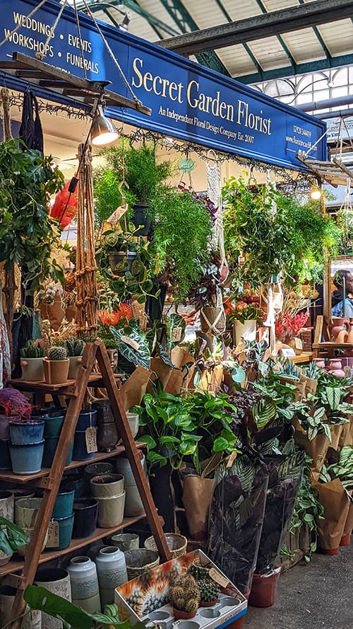 Florist market store with a number of houseplants at the front on the stand, the sign reads Secret Garden Florist