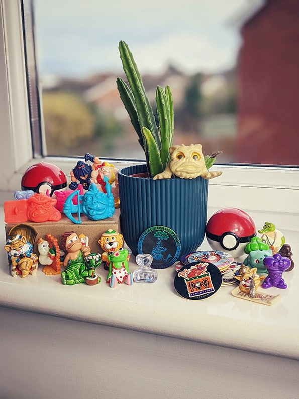 1980s and 1990s toy collection surrounding a Stapelia houseplant showing, Monster Wrestlers in My Pocket, Gogo's, Pogs, Tazos, Pokemon, Boglins, Mini boglins, and Kinder Egg collectibles